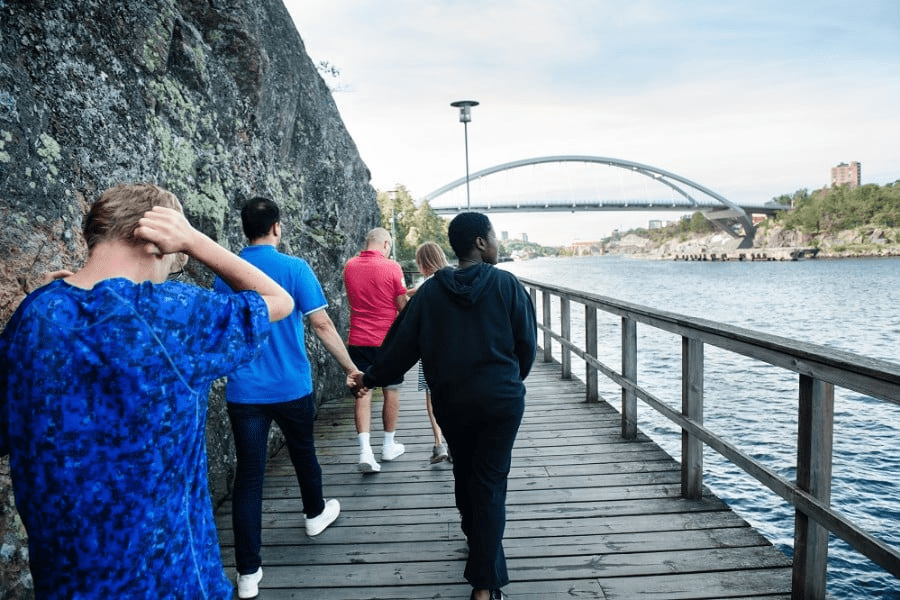 Fyra personer går en strandpromenad med berg på ena sidan och vatten på andra sidan