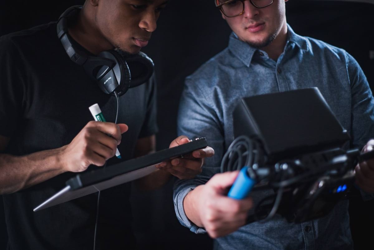 man in black tee shirt holding writing board while other man holding monitoring device.jpg