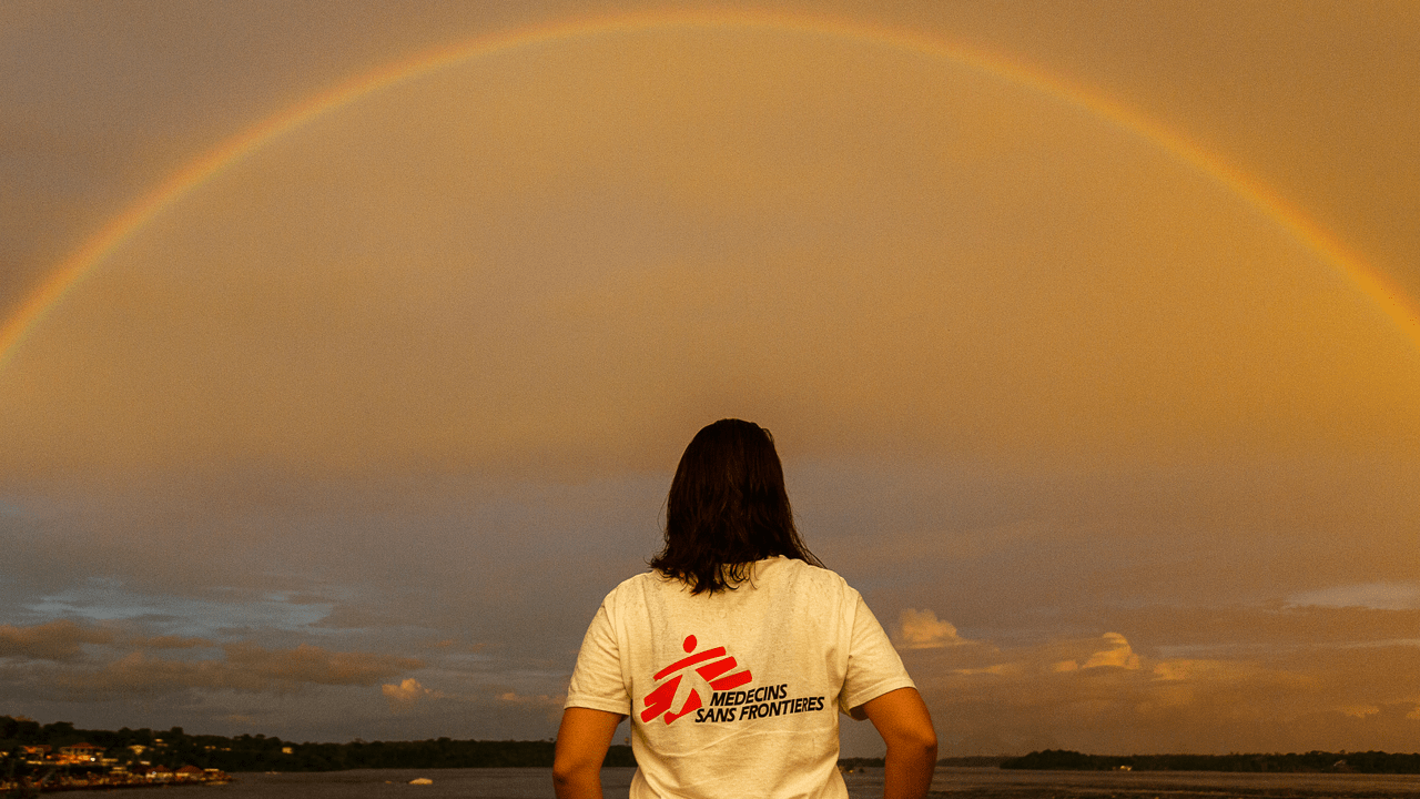 person with long hair shown from the back facing a rainbow over a field