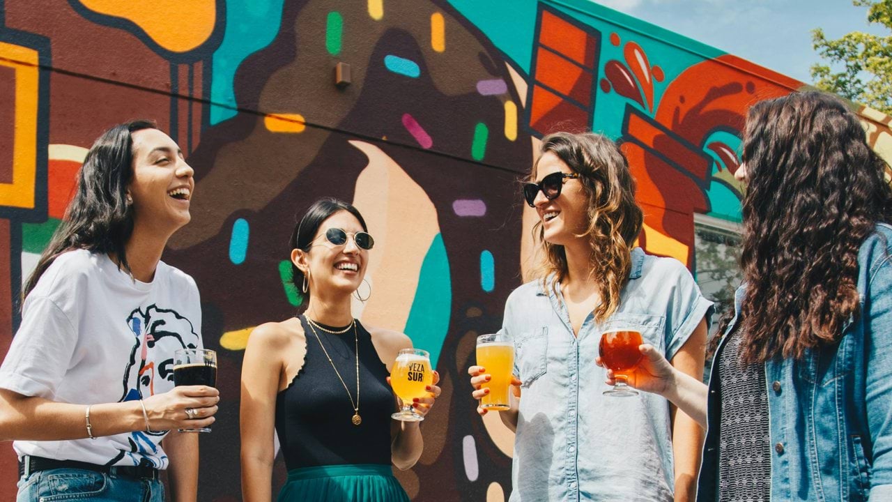four women holding drinks while laughing together during daytime