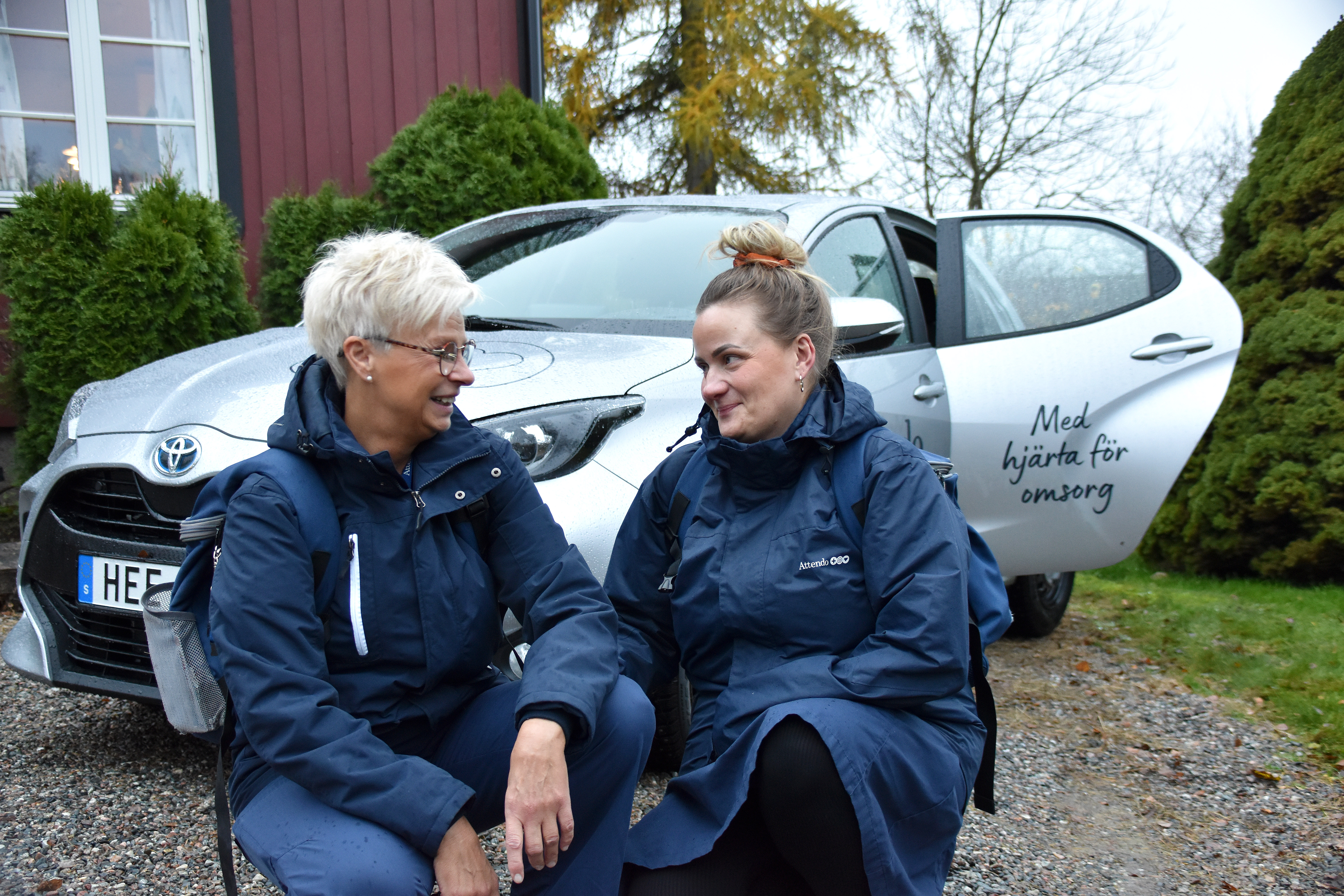 Två medarbetare i hemtjänsten framför en Attendo-bil