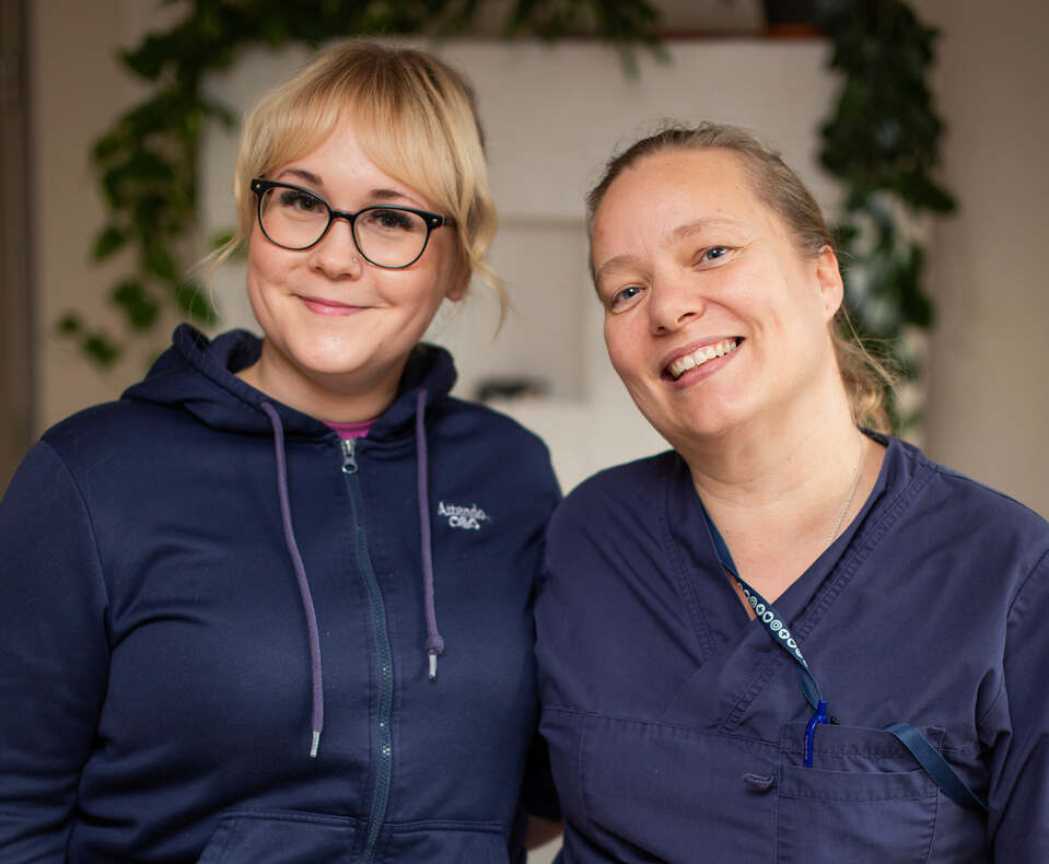 kaksi attendolaista hymyilee kameralle tummansinisissä työvaatteissa