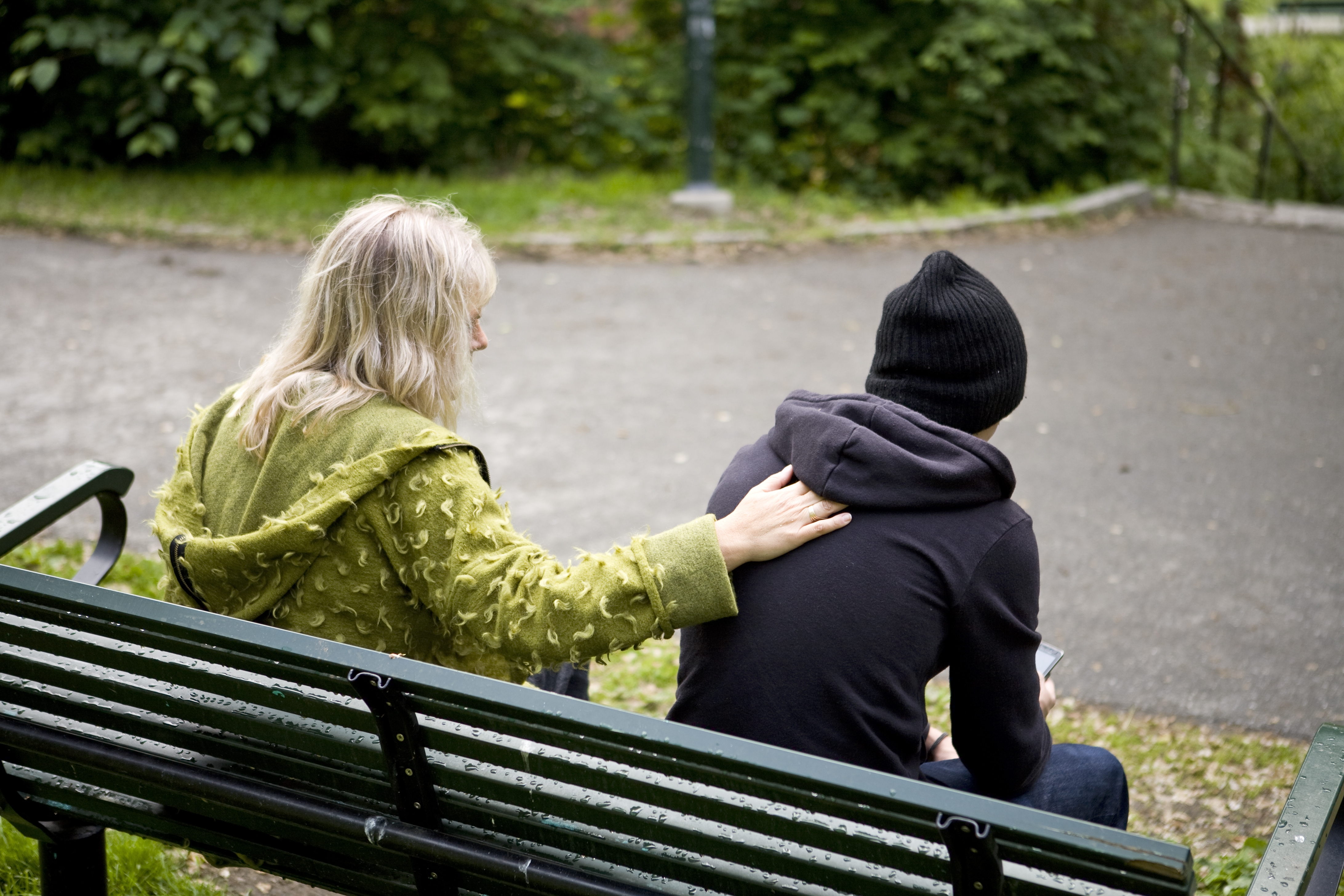 En vuxen och en ungdom sitter och pratar på en parkbänk