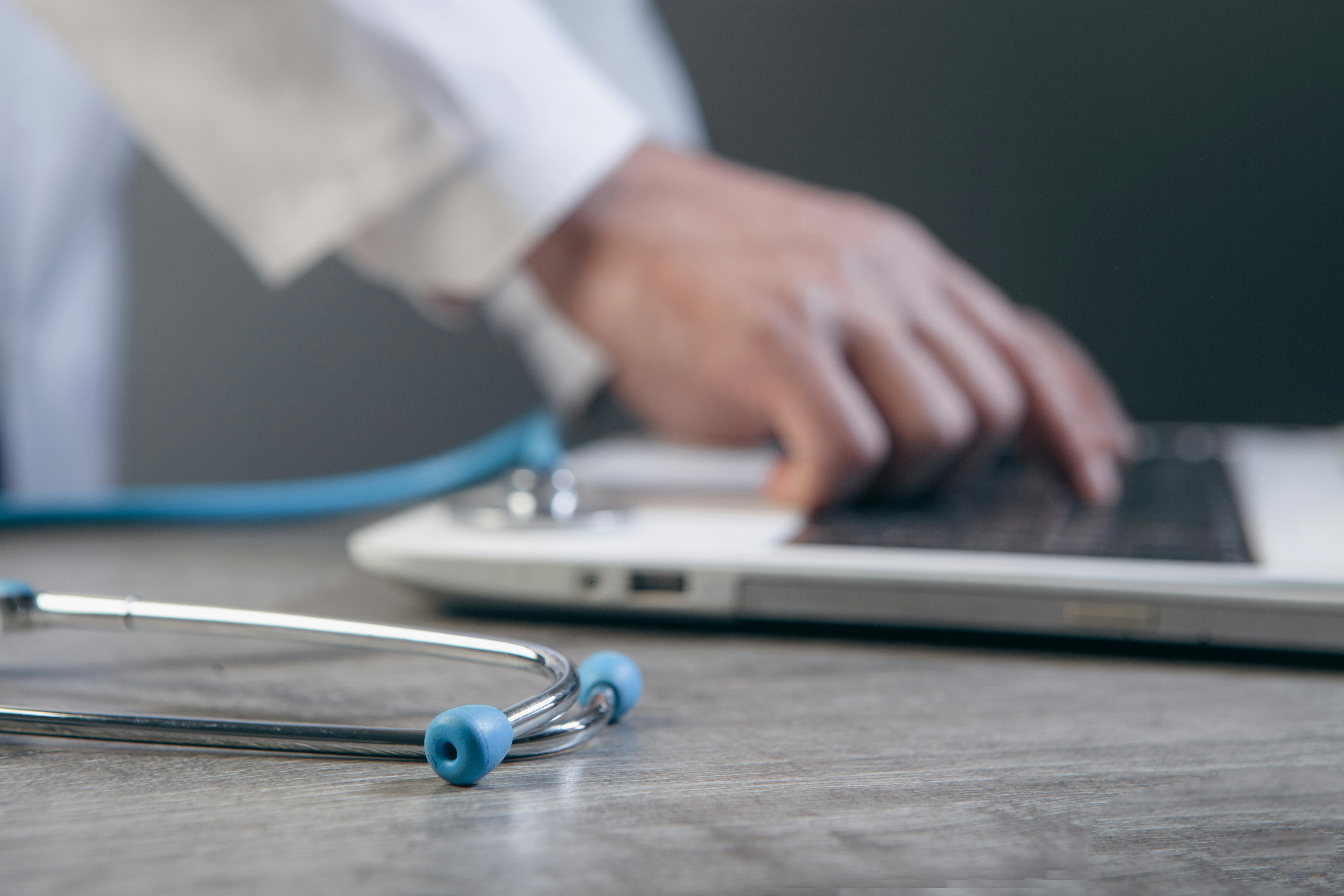 Doctor typing on a laptop with a stethoscope nearby.