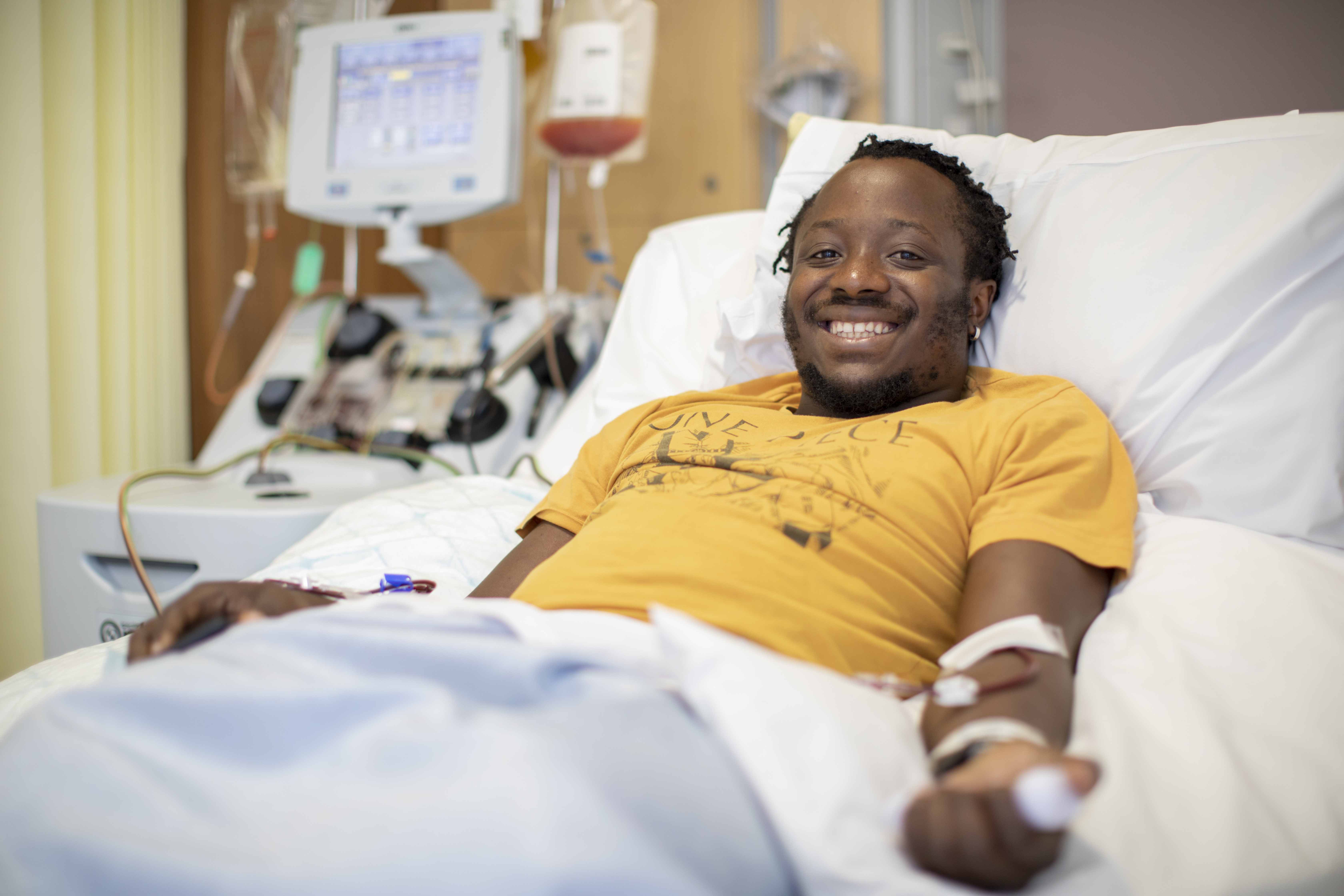 Stem cell donor smiling at camera from hospital bed whilst they donate via their blood