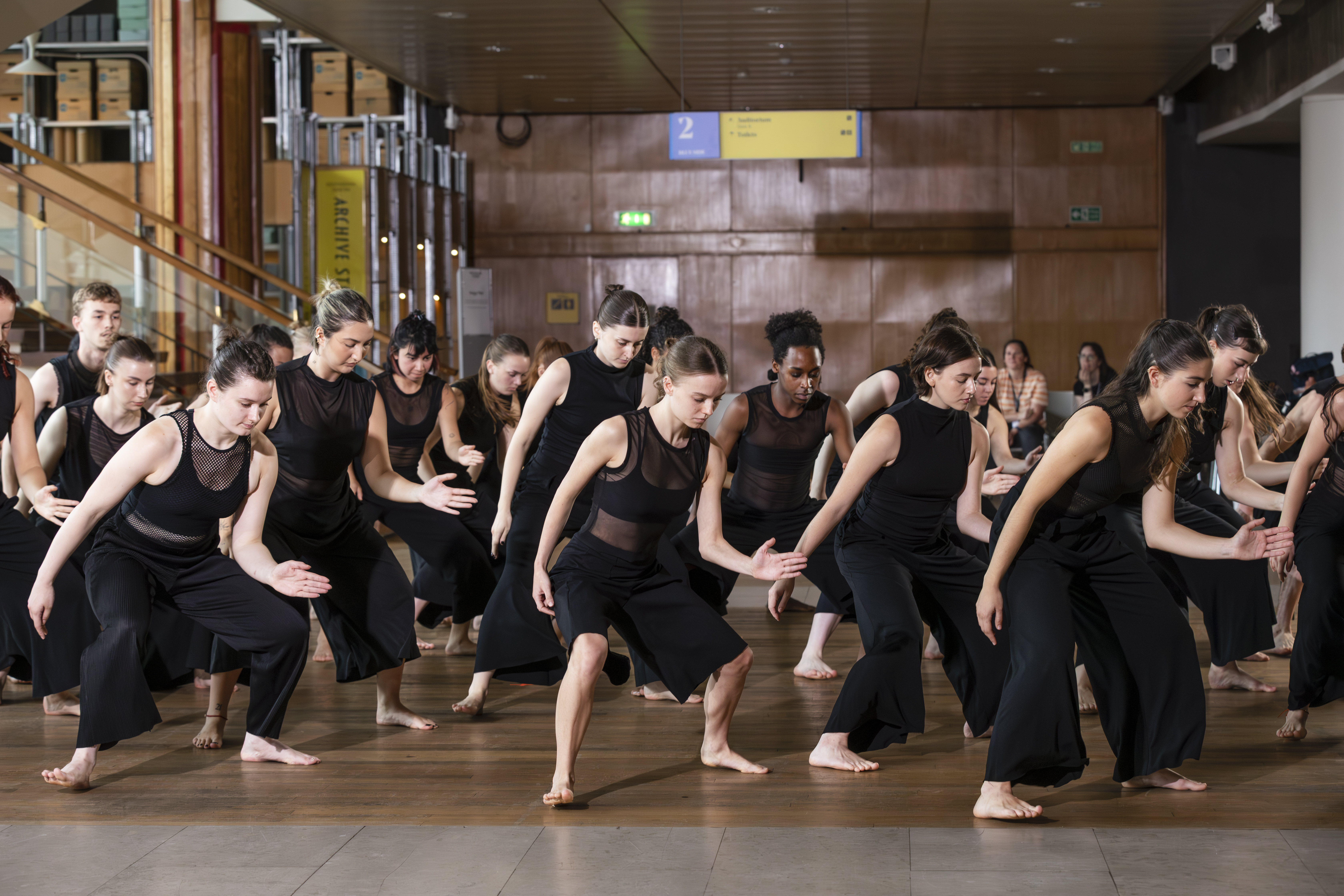 A group of dancers wearing black costumes with their left arm out in front of them in slightly bent position.