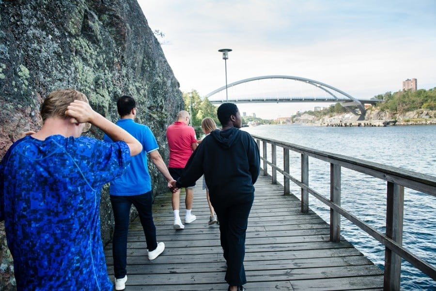 Fyra personer går en strandpromenad med berg på ena sidan och vatten på andra sidan