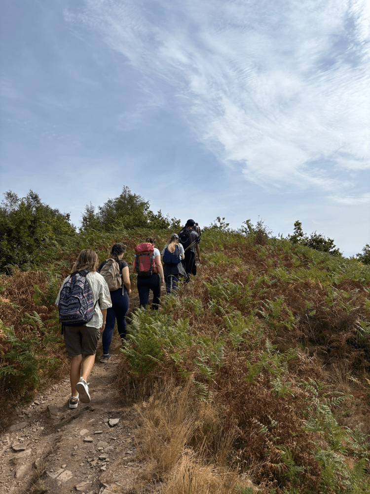 A group of people walk along a narrow trail through heathland and low vegetation under an open sky. Text reads: “Out There Award”.