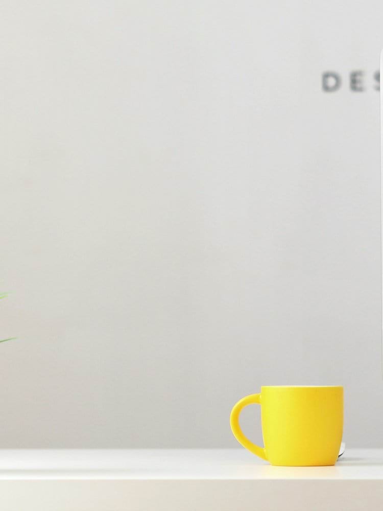 yellow ceramic mug beside gray aluminum iMac