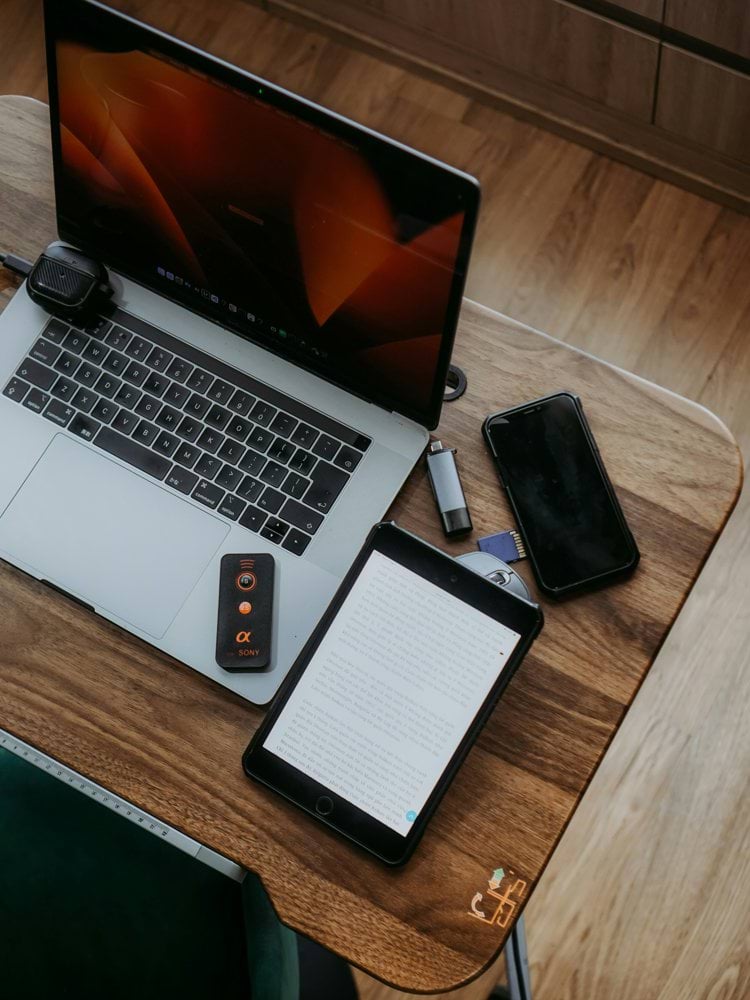 Laptop, tablet, and phone on a wooden desk.