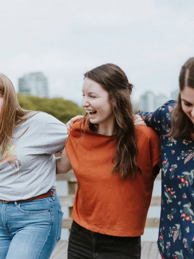 three women walking on brown wooden dock near high rise building during daytime