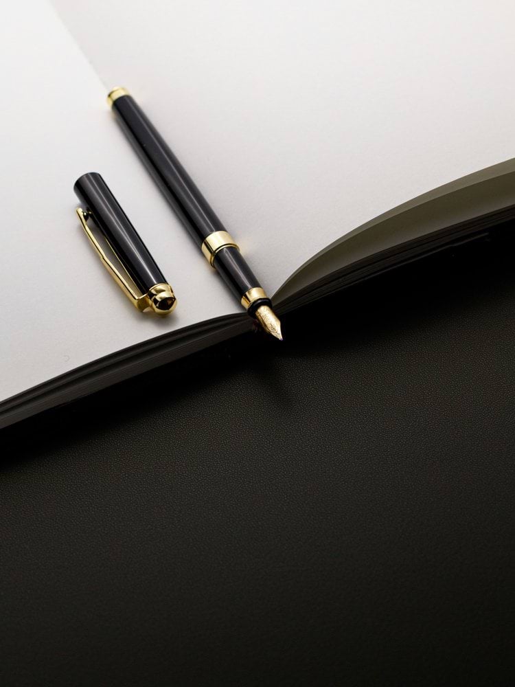 A black and gold pen rests on an open notebook.