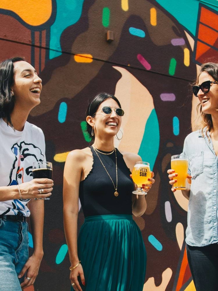 four women holding drinks while laughing together during daytime