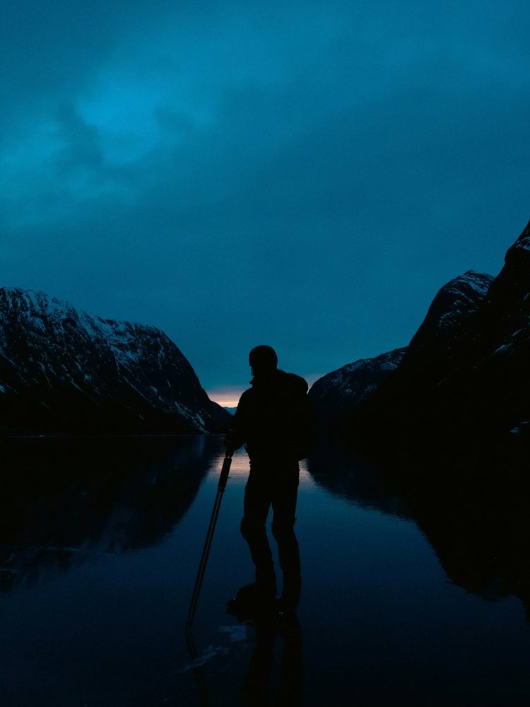 Silhouette of person standing on frozen lake at dusk