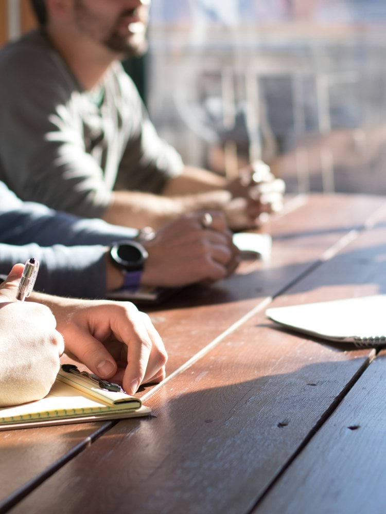 people sitting on chair in front of table while holding pens during daytime