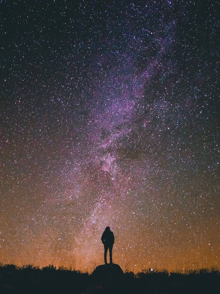 silhouette of man standing on rock while looking in sky