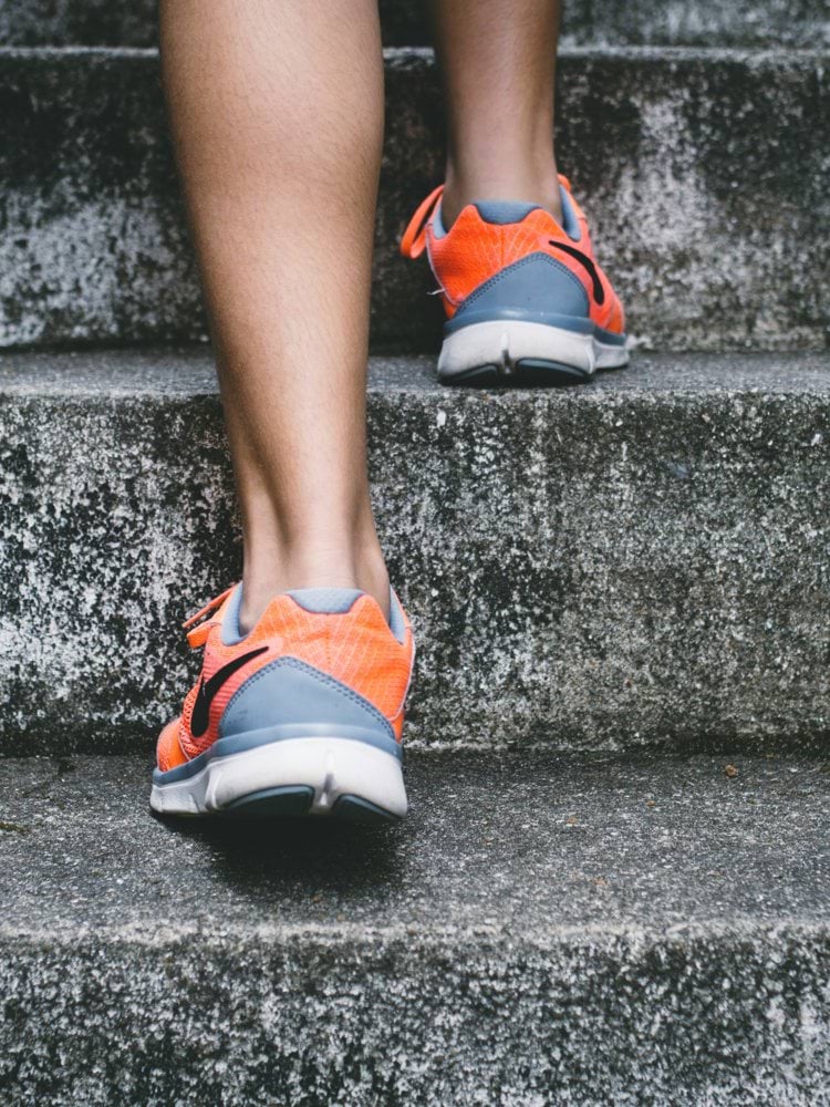 person wearing orange and gray Nike shoes walking on gray concrete stairs