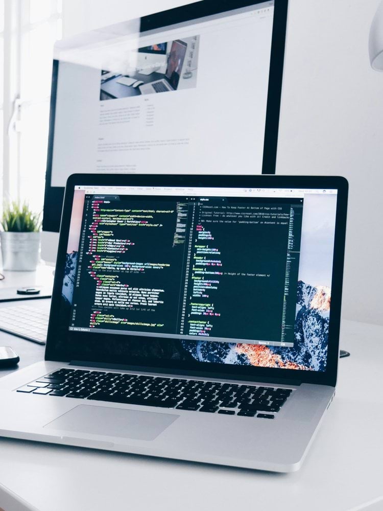 A MacBook with lines of code on its screen on a busy desk