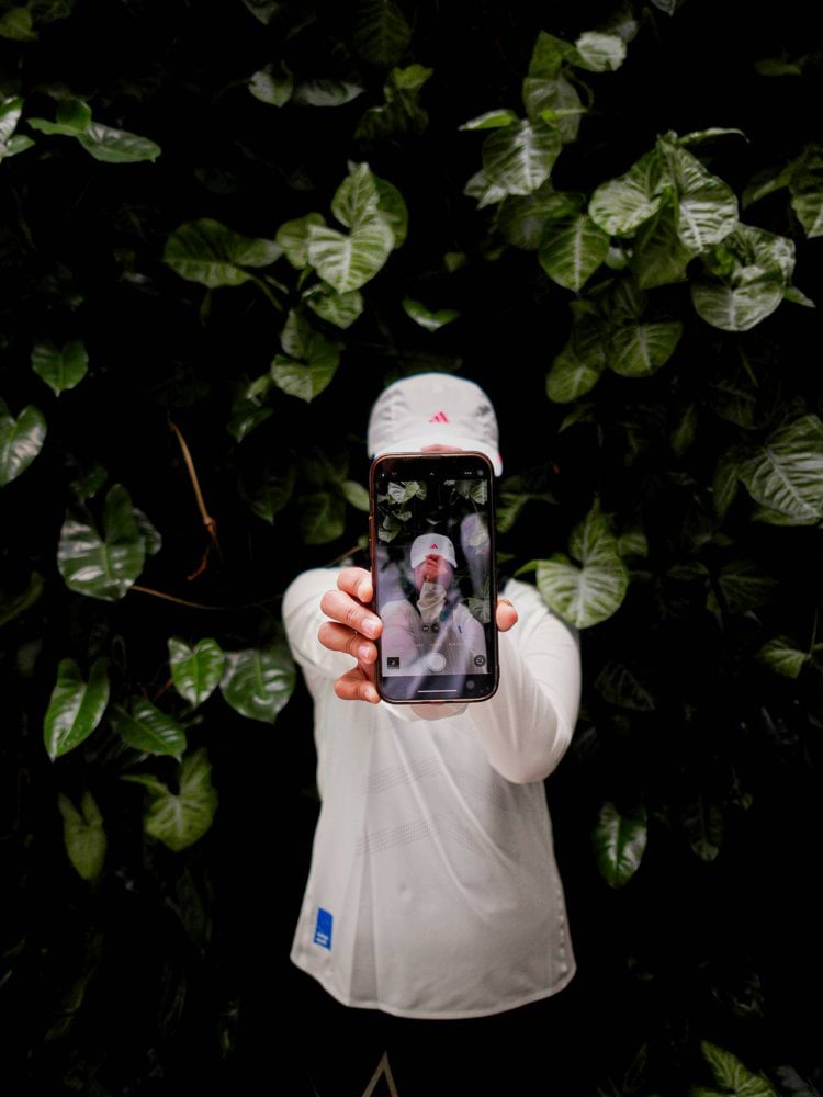 Person holding phone showing selfie with green leaves