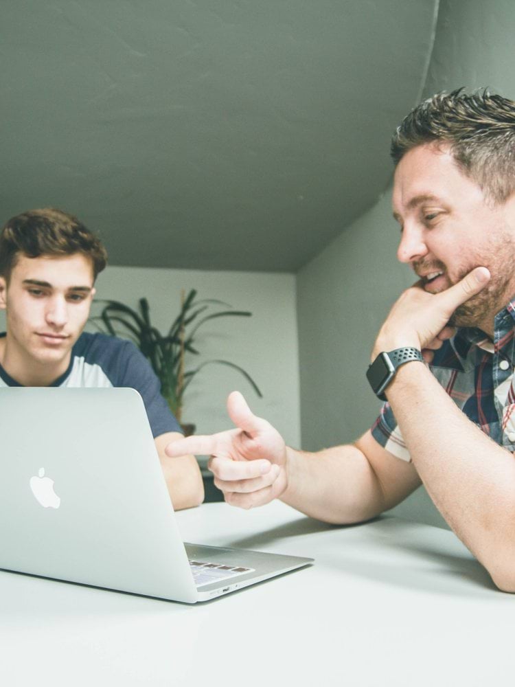man wearing white and black plaid button-up sports shirt pointing the silver MacBook