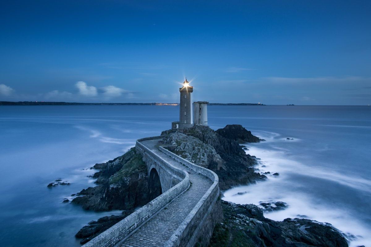 gray lighthouse on islet with concrete pathway at daytime