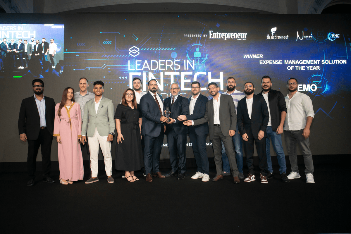 Pemo team members stand on stage at the Leaders in Fintech Awards, smiling and holding a trophy in front of a large event screen announcing their win for expense management solution of the year.