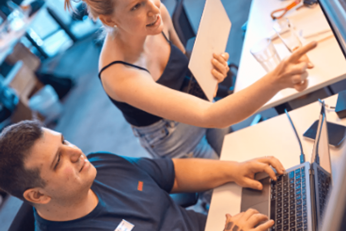 Woman standing and pointing at a computer screen while discussing something with a seated male colleague