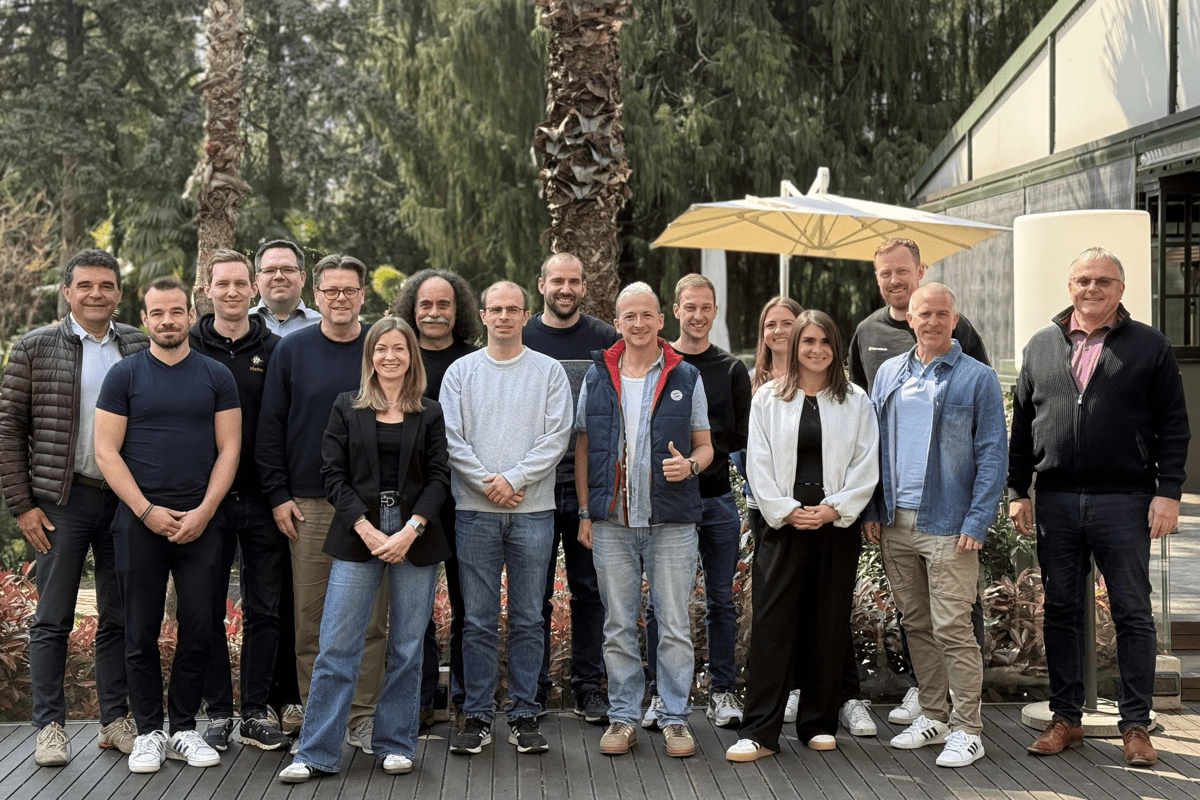 Ein Gruppenfoto von 16 Menschen im Freien vor einem Gebäude