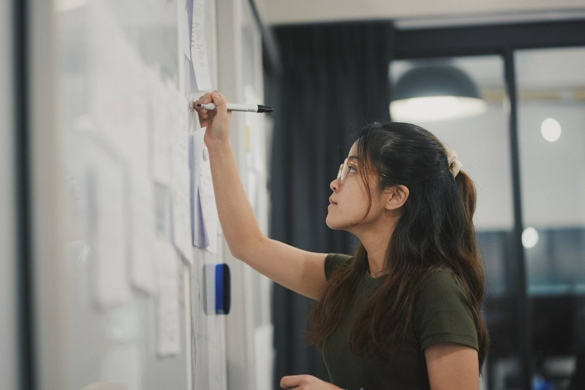 a woman writing on a white board with a marker