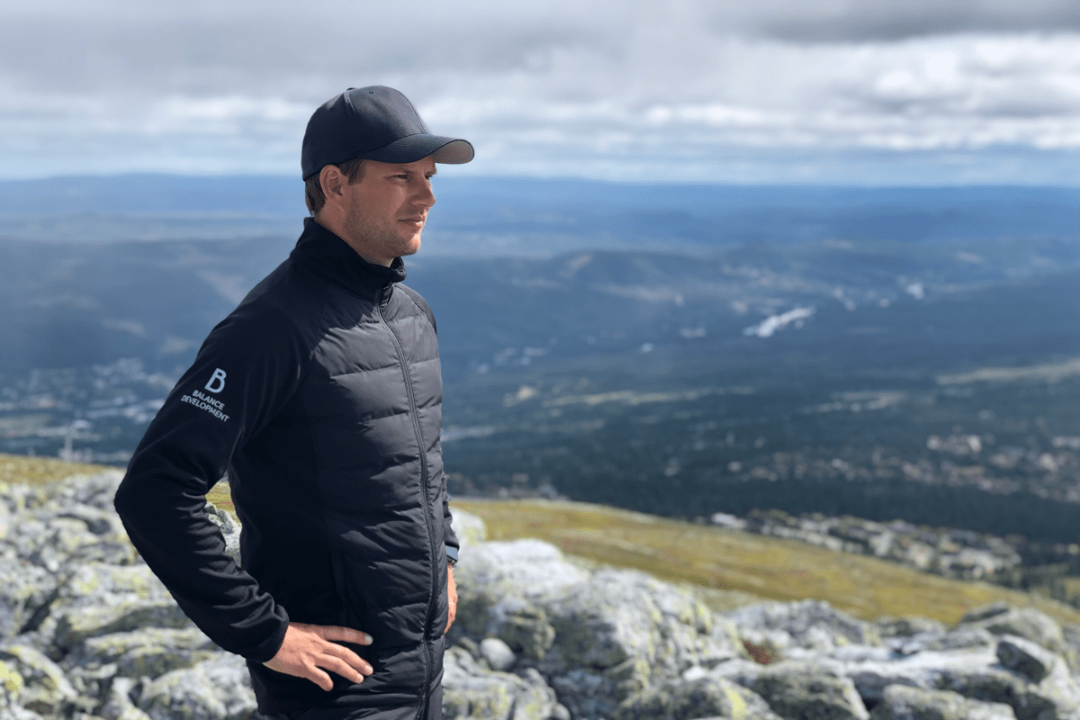man on a mountatin, wearing a dark jacket, blue sky, clouds