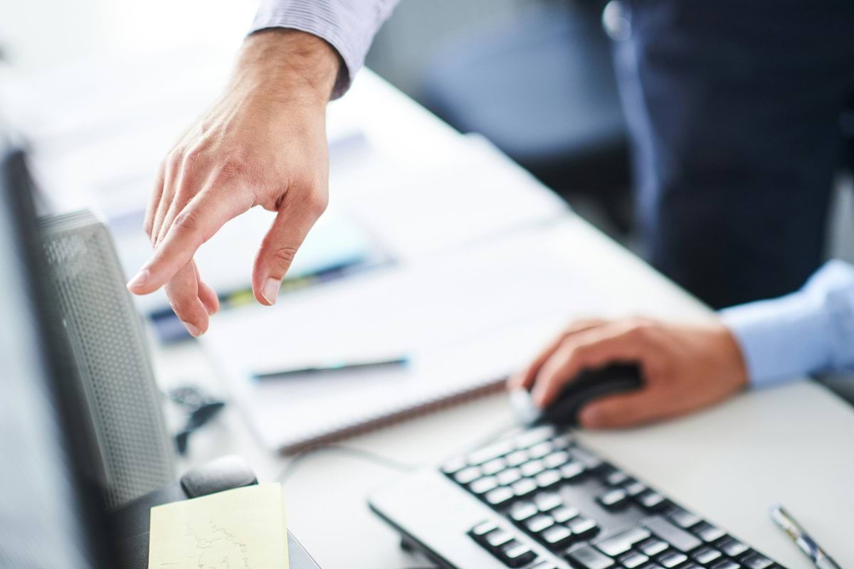 Hands pointing at computer monitor while operating mouse and keyboard