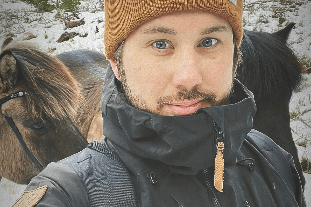 Selfie utomhus i snölandskap, person i brun mössa tittar in i kameran.