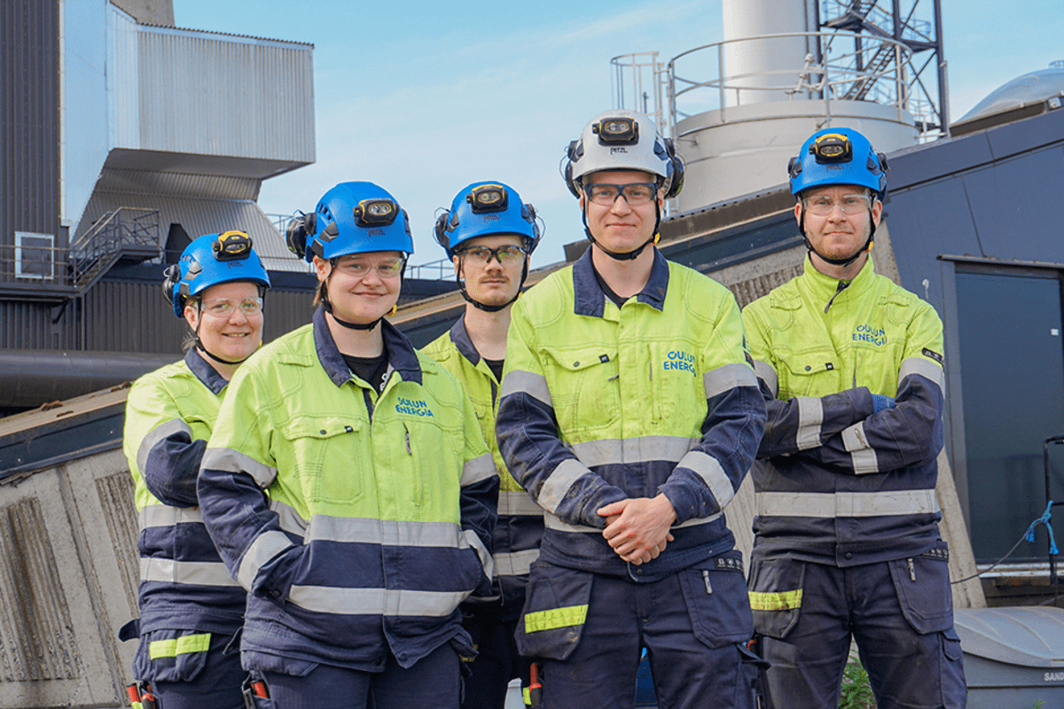 Viisi kunnossapidon kesätyöntekijää seisoo voimalaitoksen pihalla ryhdikkäästi. 