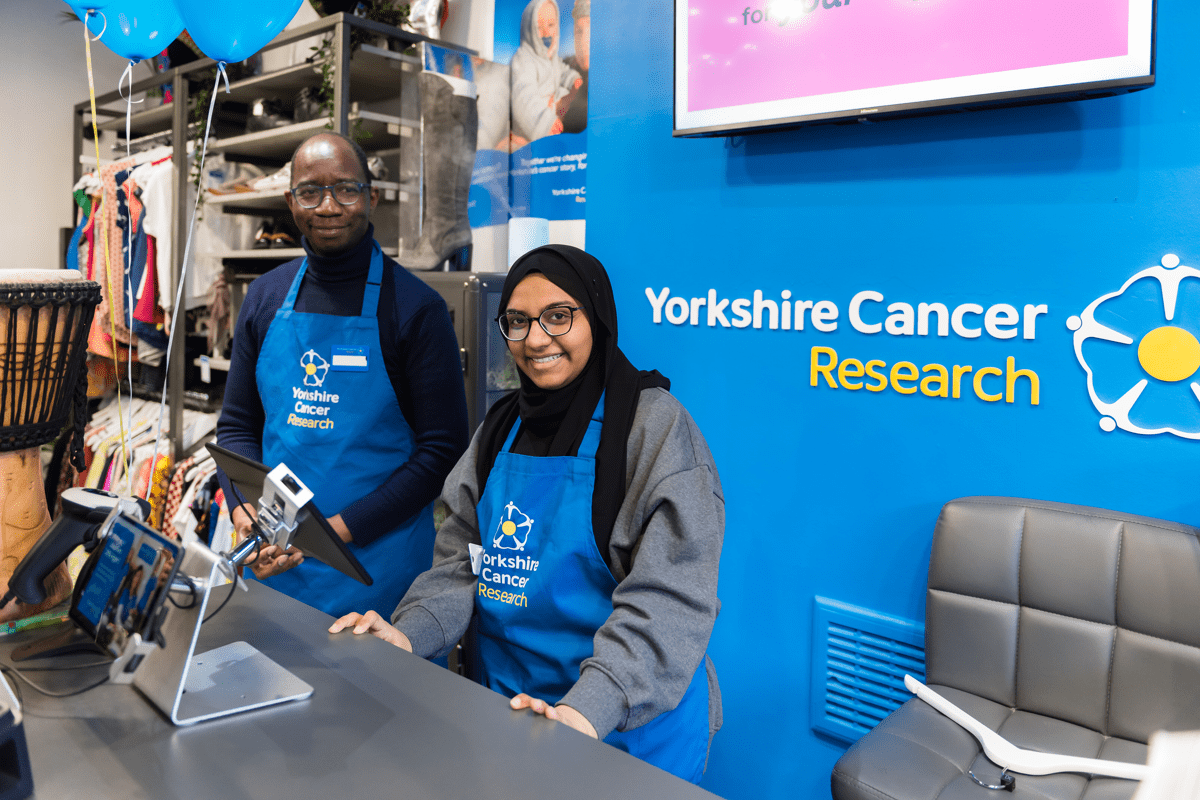 A man and woman in Yorkshire Cancer Research aprons stand behind a till