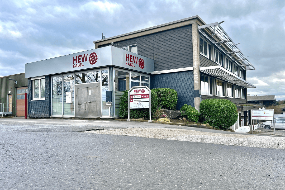 Das Bild zeigt das Firmengebäude von HEW-KABEL mit grauer Fassade, großen Fenstern und dem Firmenlogo.