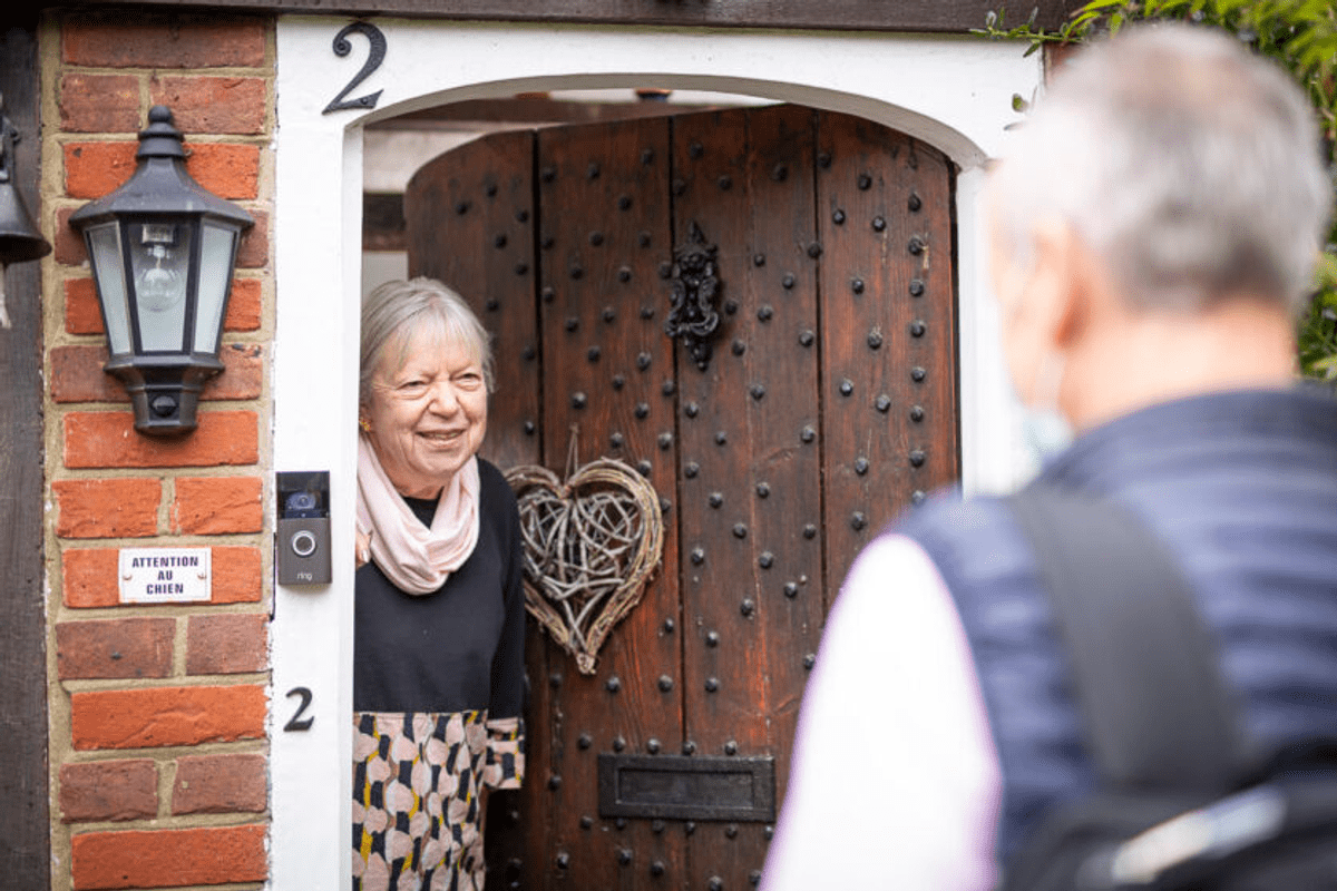 A woman at the front door, and a person approaching the door. She looks happy to see him.