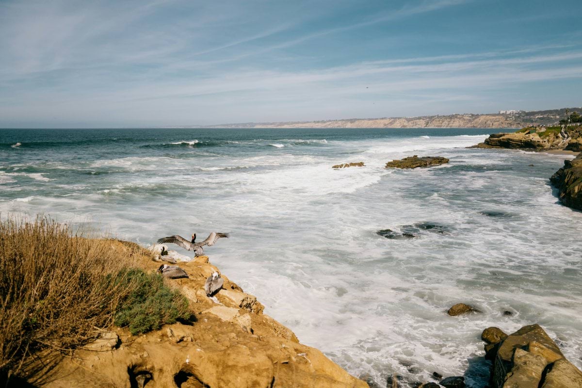 Waves crash on a rocky coastline under a blue sky.