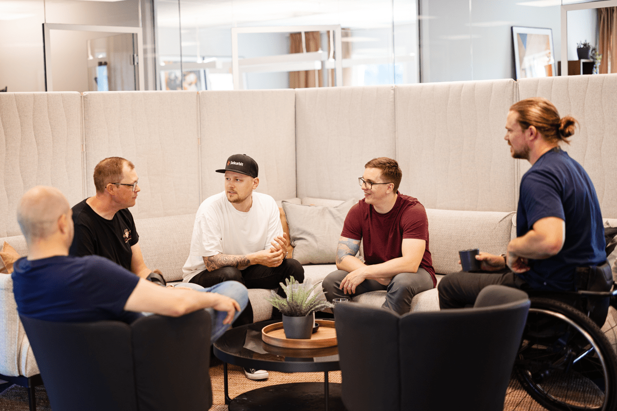 Fem personer sitter i en avslappnad grupp i en lounge-miljö och samtalar. 