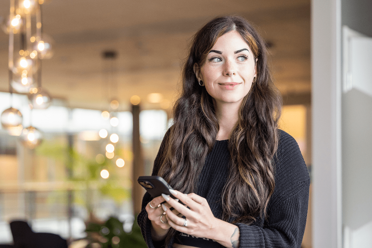 Medarbetare håller mobil i handen och tittar leende bort.