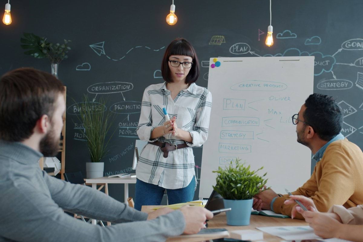Woman presents to colleagues at a whiteboard meeting.