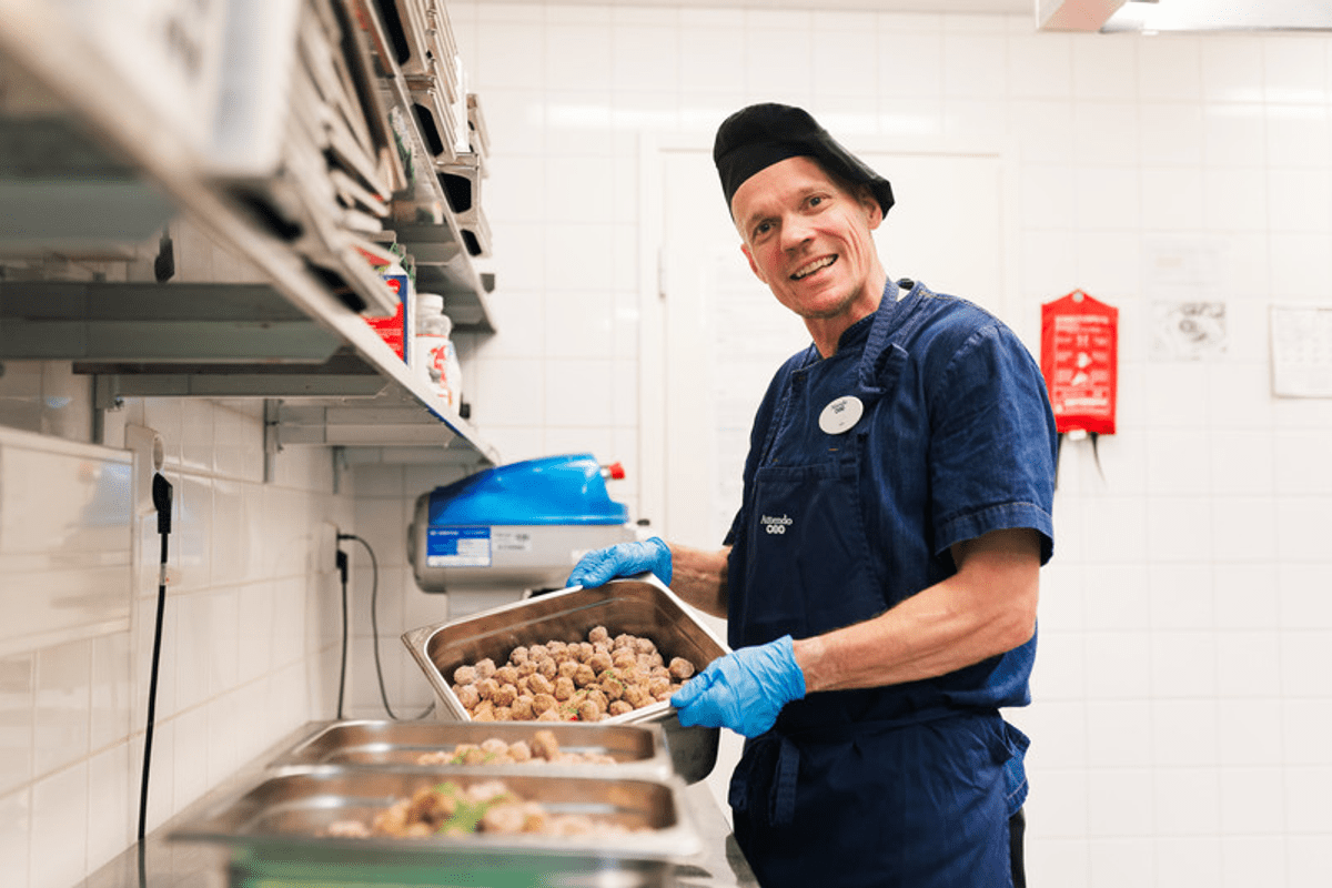 Attendon kokki katsoo hymyilevänä kameraan ja valmistelee lihapullia uuniin laittoa varten