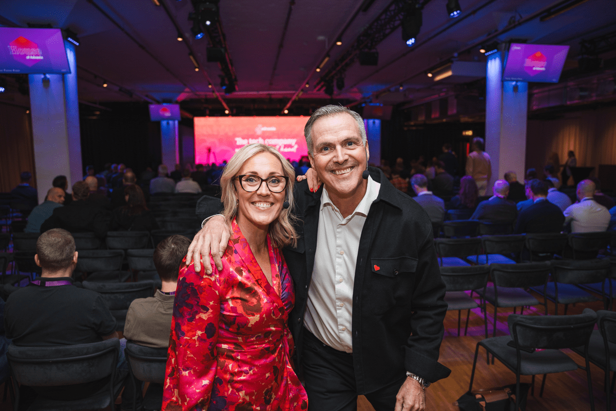 Två personer poserar tillsammans i konferenslokal med publik.