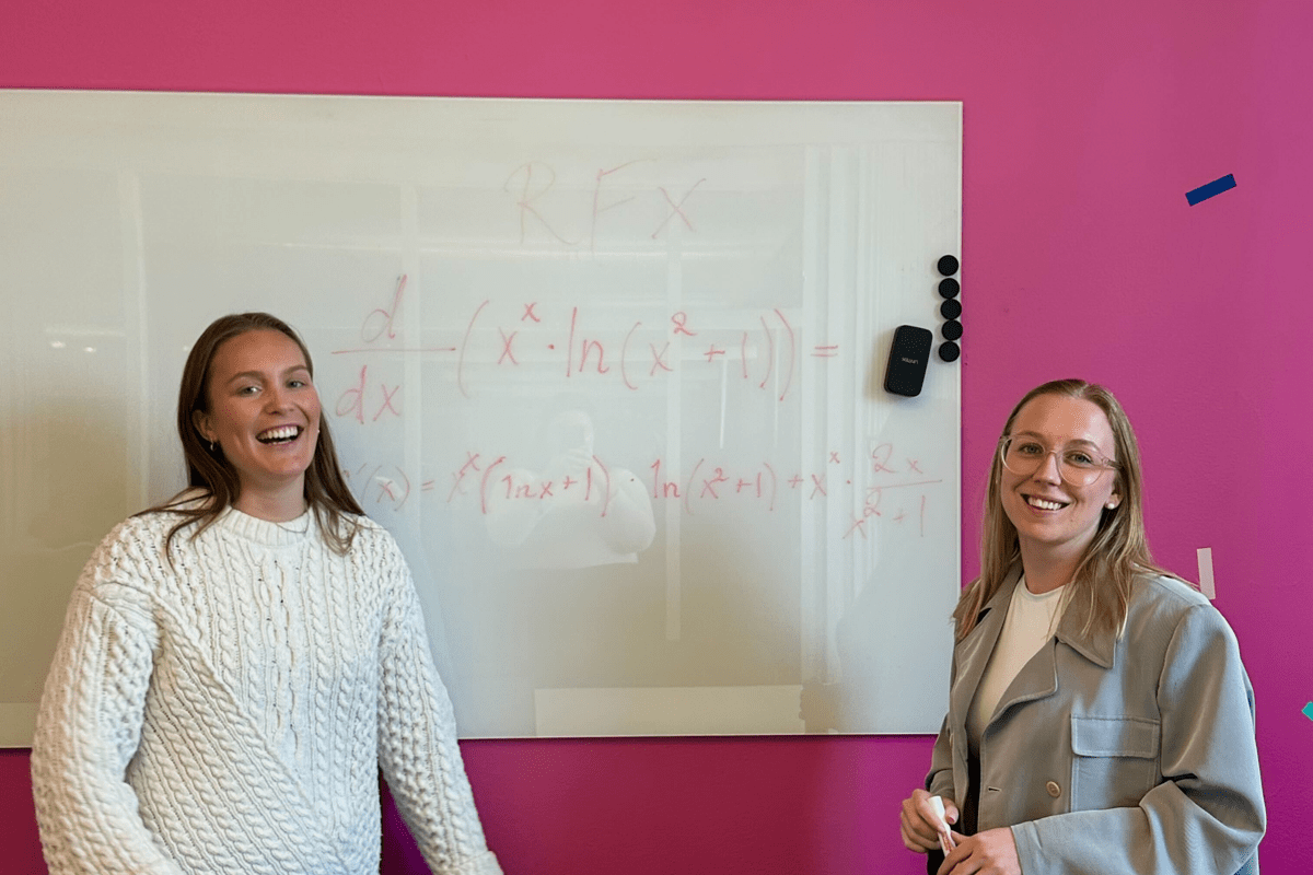 Two people standing in front of a whiteboard with maths on it