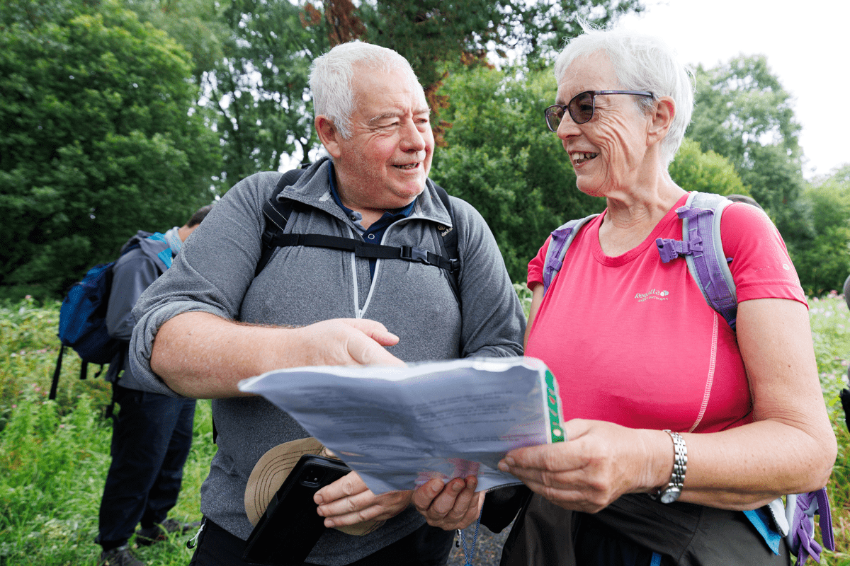Two walkers look at a map together on a countryside path, while other members of the group stand nearby.