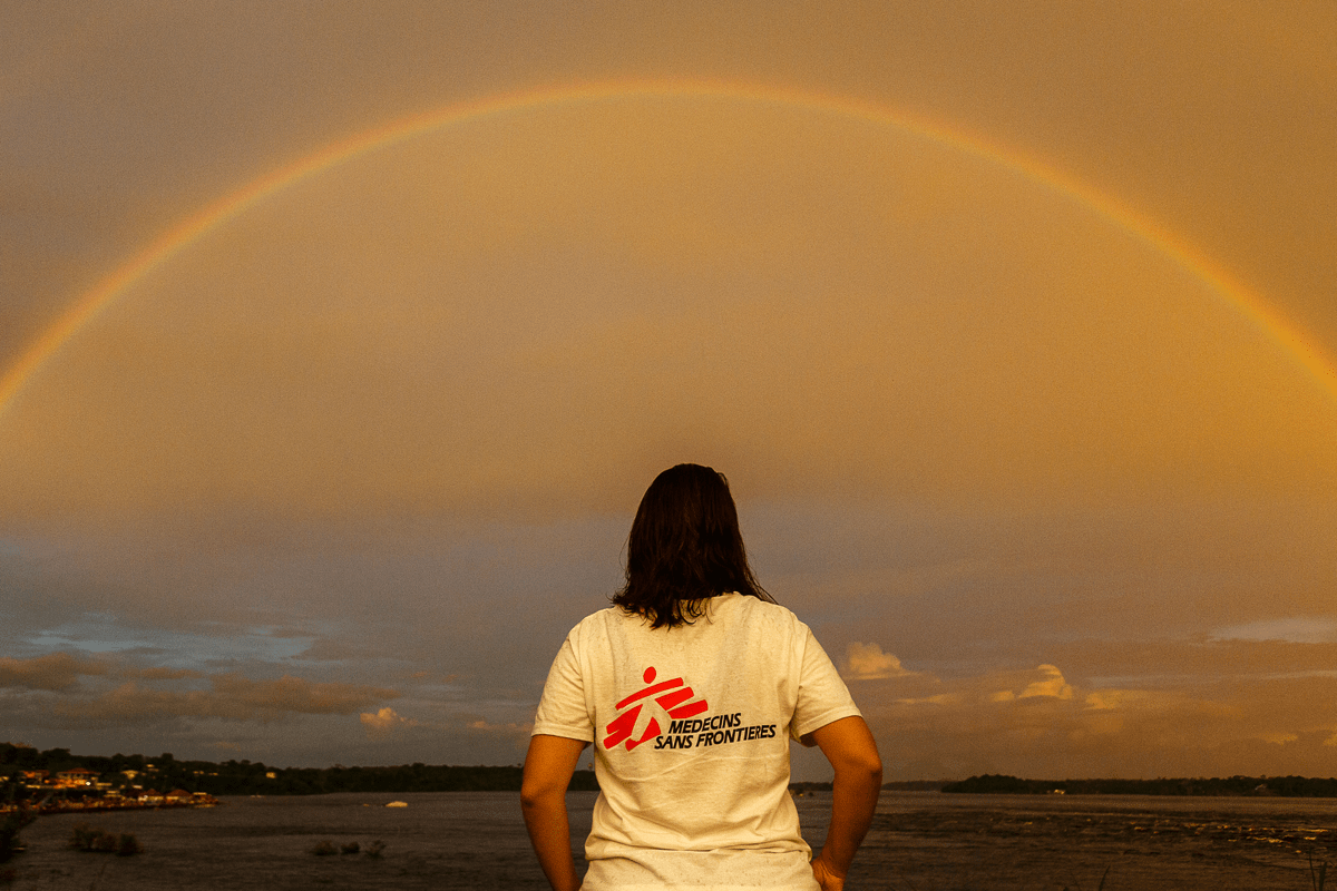 person with long hair shown from the back facing a rainbow over a field