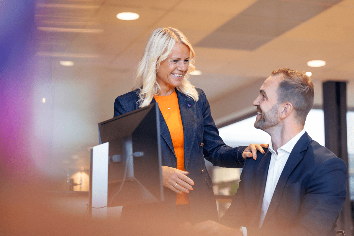 Kvinna står och pratar med sittande kollega vid bord.