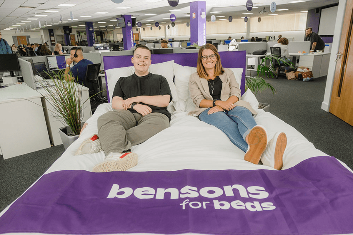Man and woman smiling sat on a bed 