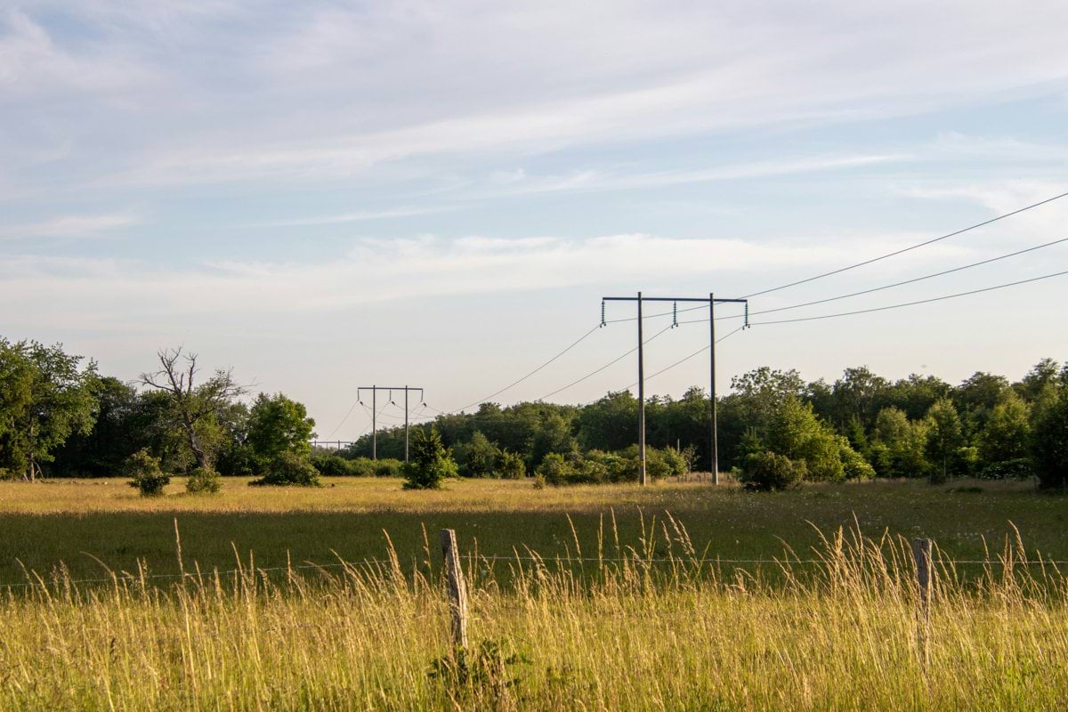 green grass field near electric posts under white clouds during daytime