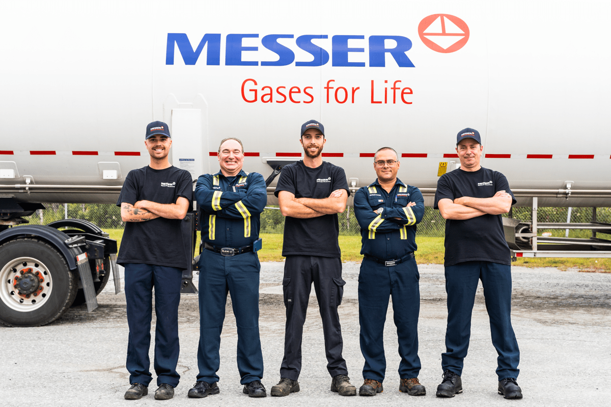 Five men standing with arms crossed in front of a large tanker truck with the logo 'Messer Gases for Life'