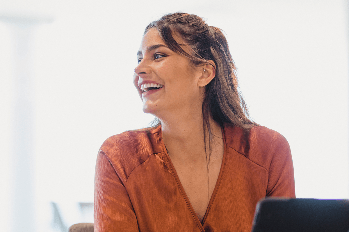 Woman wearing a burnt orange shirt smiling in front of a laptop. 